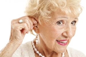 Closeup of a senior woman inserting a hearing aid in her hear.  Focus on the hearing aid.